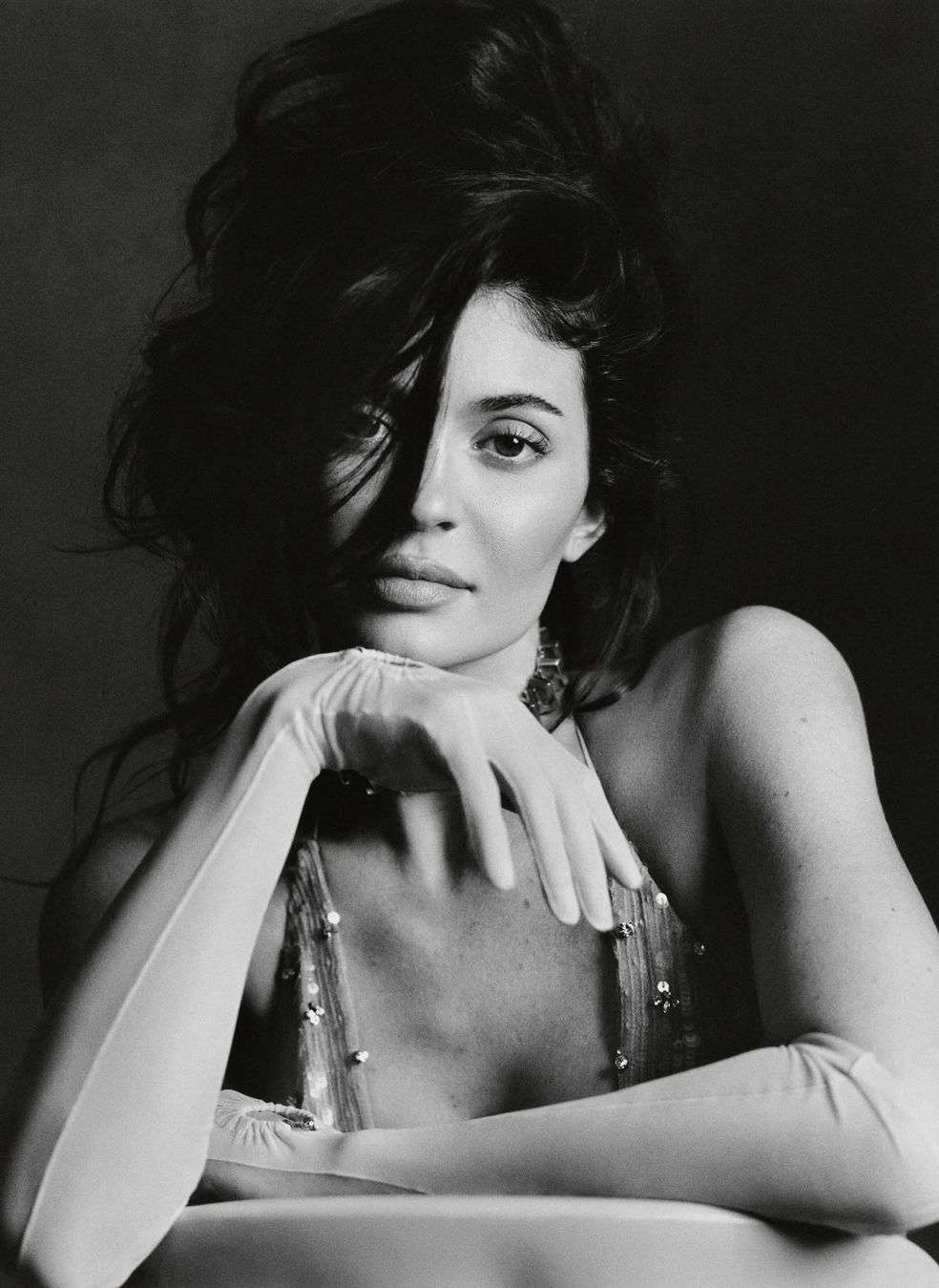 Black-and-white portrait of a woman with voluminous dark hair, wearing formal gloves, posing in front of a dark background.