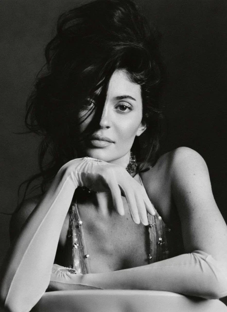 Black-and-white portrait of a woman with voluminous dark hair, wearing formal gloves, posing in front of a dark background.