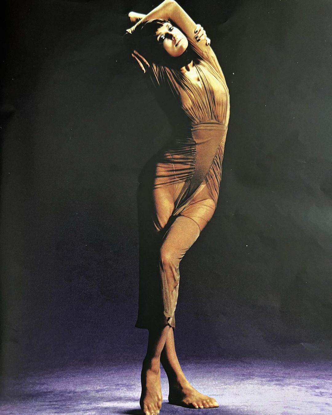 Model in a sheer pleated dress posing against a dark gradient studio background by Luis Alberto Rodriguez.