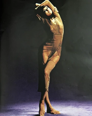 Model in a sheer pleated dress posing against a dark gradient studio background by Luis Alberto Rodriguez.