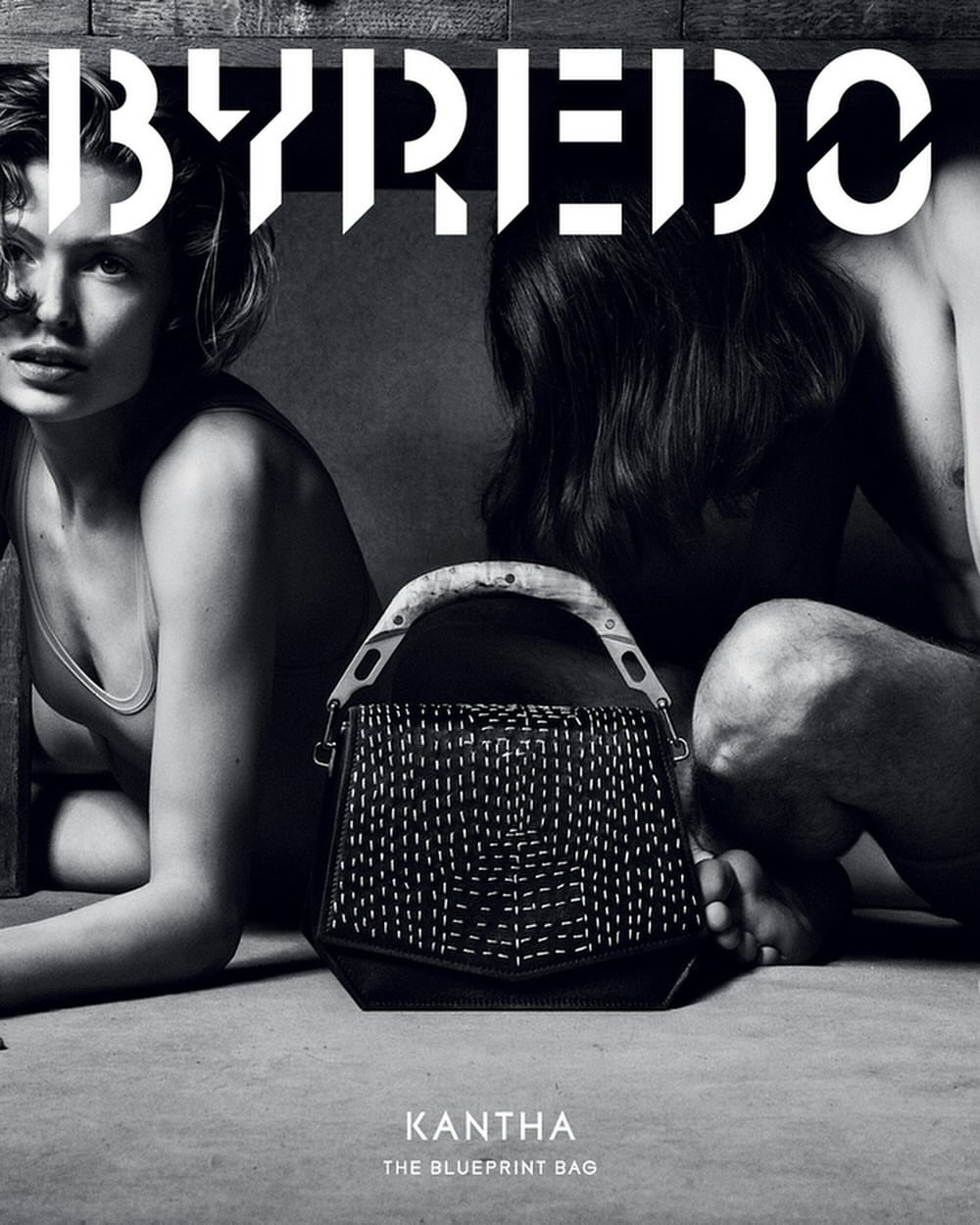 Byredo campaign features a black leather Kantha bag with white stitching between two models in a neutral setting, showcasing fashion and design.
