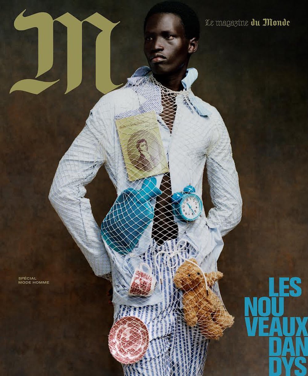 Magazine cover featuring an adult Black male model in a white and blue patterned shirt and striped pants, accessorized with vintage items.