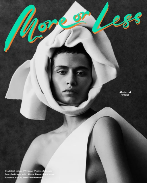 Fashion editorial shot of a person with bare shoulders, head wrapped in white fabric, wearing white clothing, against a grey backdrop.