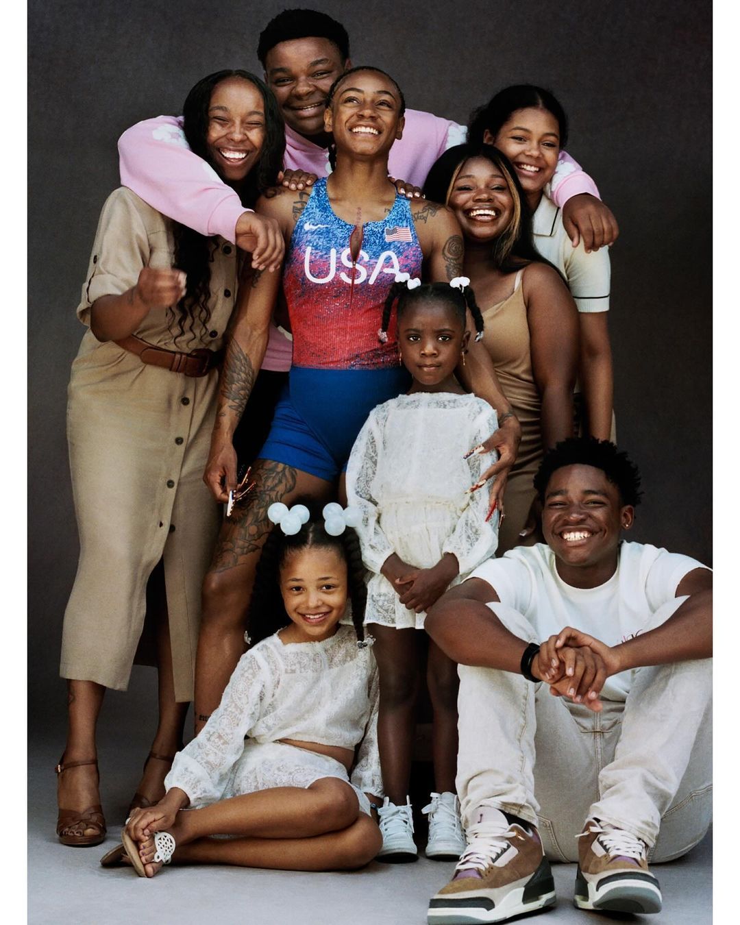 Group portrait of eight smiling people of mixed ages and ethnicities in a photo studio with a neutral gray background.