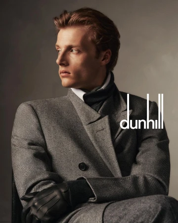 Portrait of a fair-skinned adult male model in a grey overcoat and black leather gloves, looking off to the side in soft light.