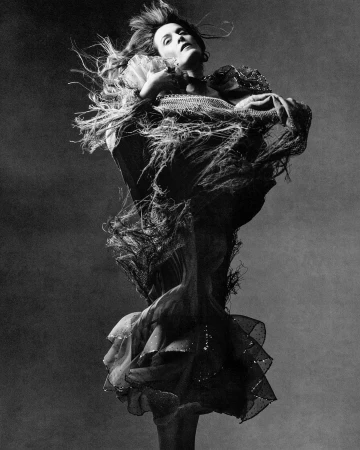 Model in dynamic motion wearing a textured ruffled dress against a dark textured backdrop by Luis Alberto Rodriguez