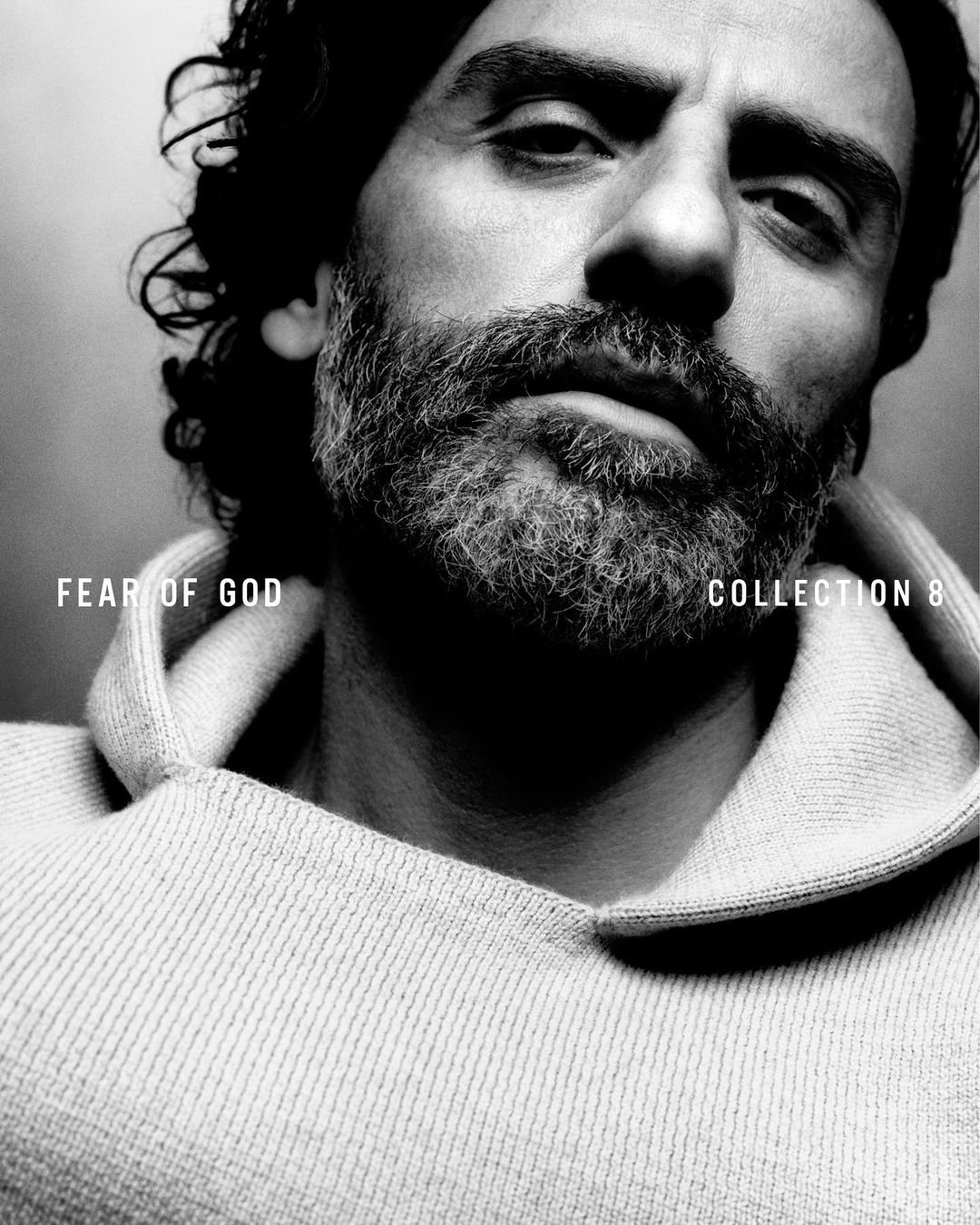 Black and white portrait of a bearded adult male wearing a hooded sweatshirt, with the text “Fear of God COLLECTION 8” visible.
