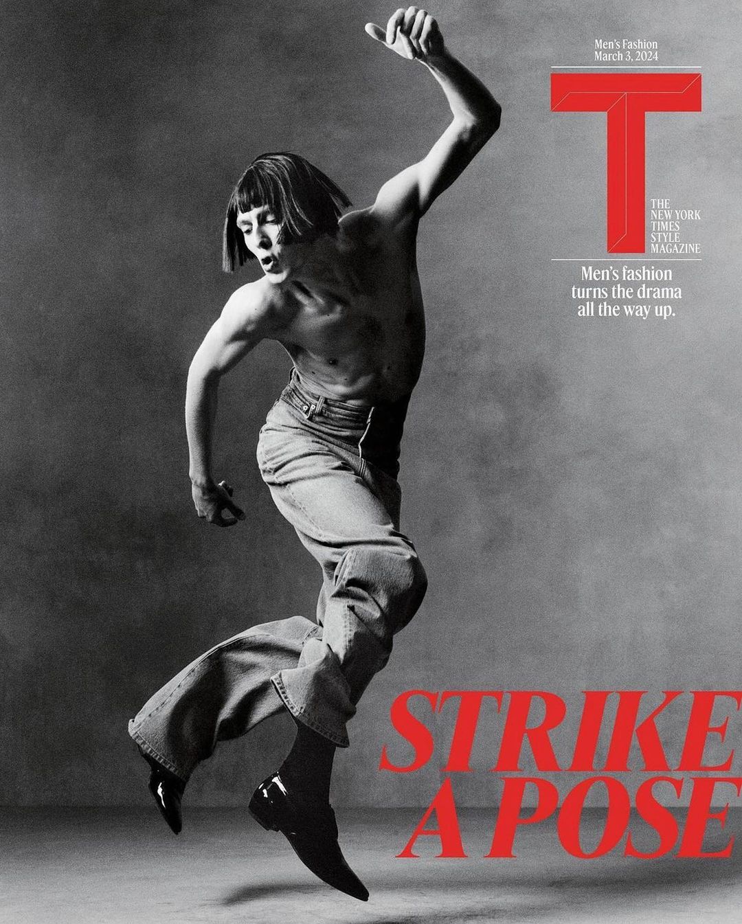 Black and white magazine cover shot of a male fashion model striking a dynamic pose in wide-leg jeans and dress shoes on gray background.