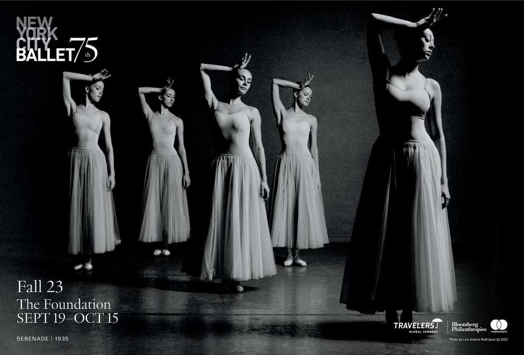 Five ballet dancers pose in pale tutus against a dark gray background in this black-and-white dance performance shot.