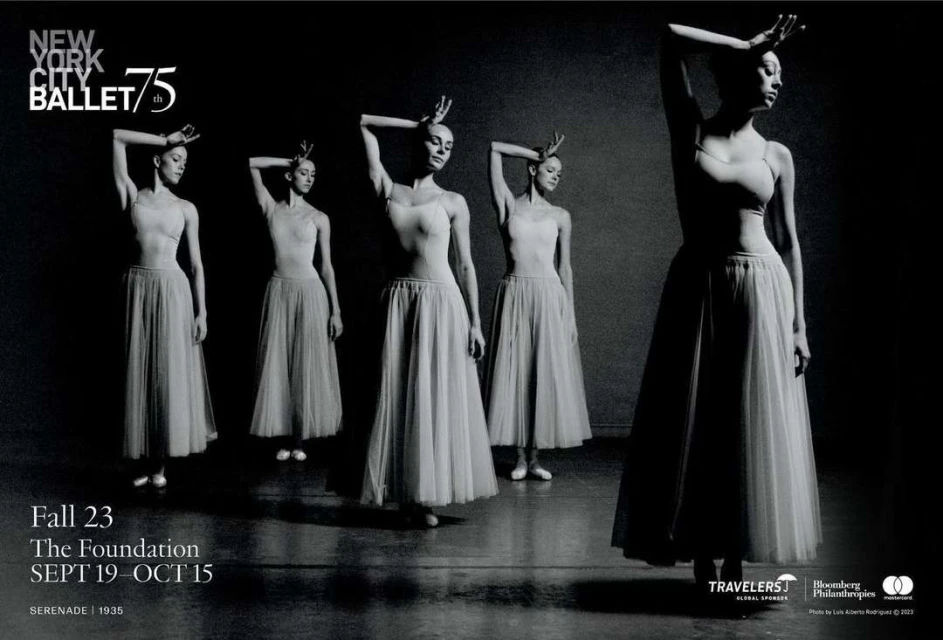 Five ballet dancers pose in pale tutus against a dark gray background in this black-and-white dance performance shot.