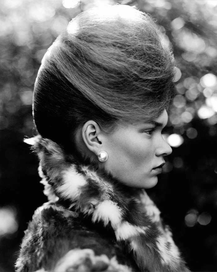 Monochrome profile portrait of a woman with voluminous beehive hair wearing a patterned fur collar and pearl earring