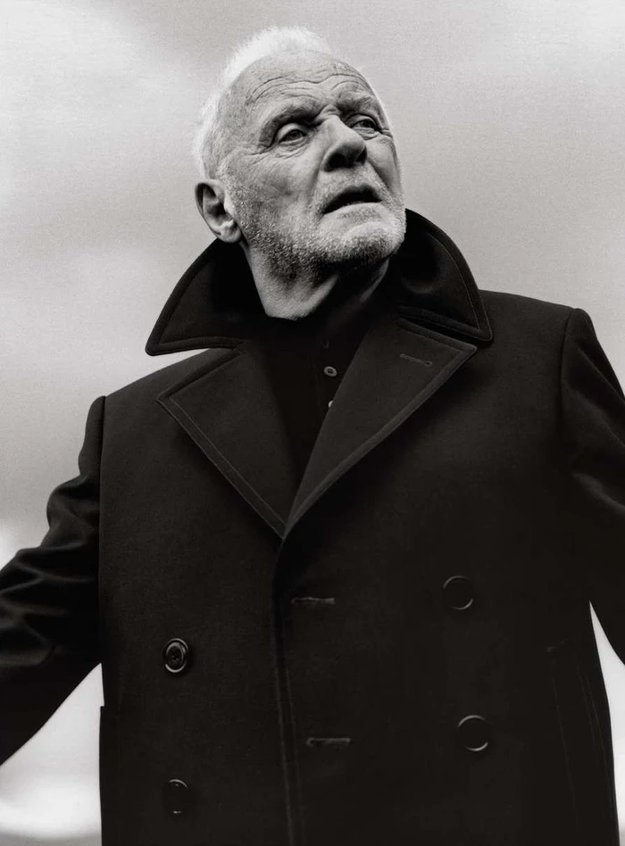 Portrait of Anthony Hopkins wearing a dark double breasted coat against a plain background