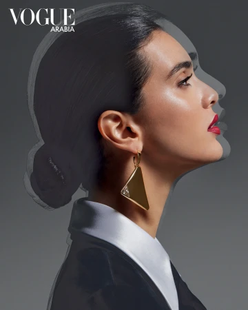 Profile portrait of a woman wearing statement gold geometric earrings and a black jacket with a white collar.