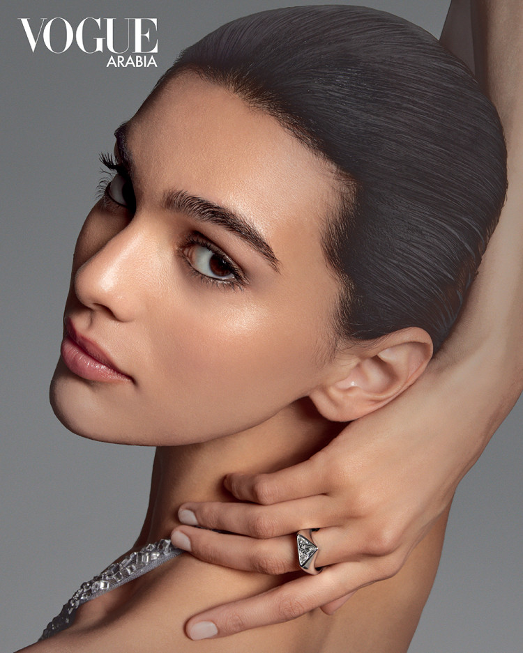 Close-up portrait of a woman with slicked-back dark hair wearing a silver ring against a grey background