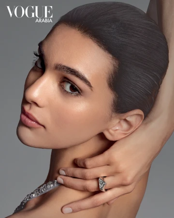 Close-up portrait of a woman with slicked-back dark hair wearing a silver ring against a grey background