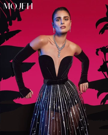 Taylor Hill wearing a black strapless gown with silver embellishments and long black gloves against a magenta backdrop