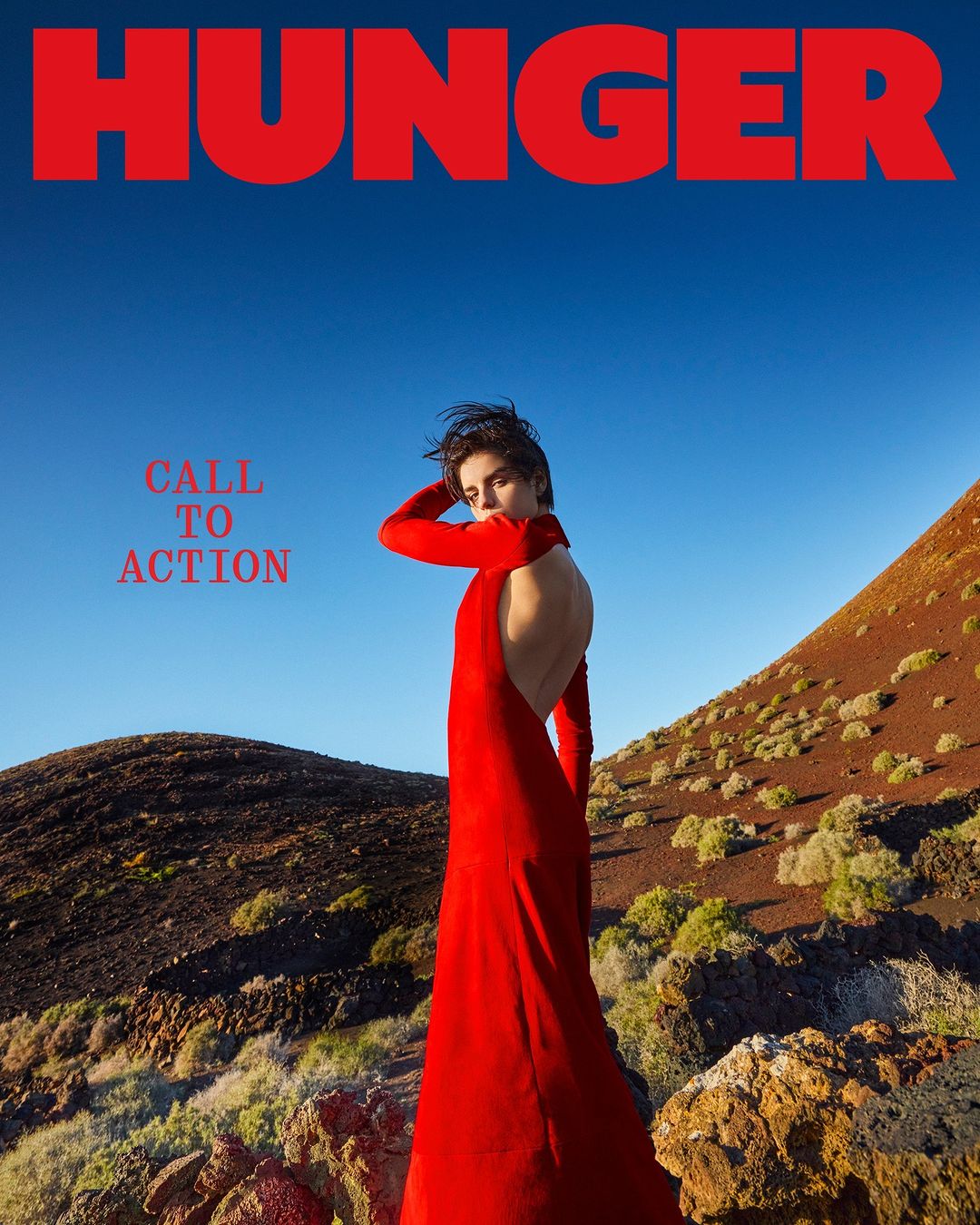 Fashion editorial cover for Hunger magazine, featuring a woman in a red dress against a backdrop of clear blue sky and volcanic landscape.