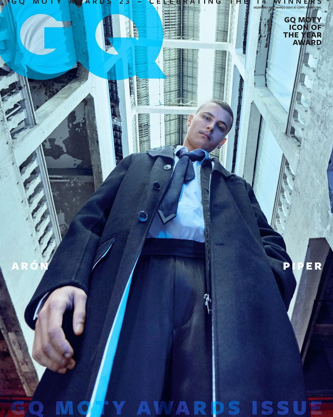 GQ Magazine cover featuring a male model wearing a dark coat and tie, photographed from a low angle against a structural background.