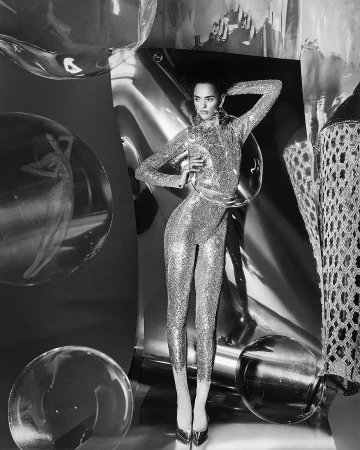 Monochrome portrait of a woman in a sequined jumpsuit posing with a hand on her hip surrounded by metallic and transparent orbs.