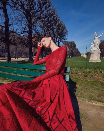 Model in a red dress seated on a green park bench under clear blue sky shot by Luis Monteiro in Milan