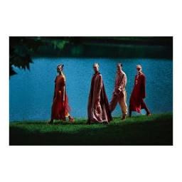 Four models walking in a line across a grassy bank beside a blue lake, photographed by Luis Sanchis.