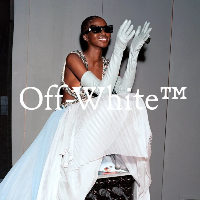 Runway fashion: A Black female model in an embellished dress and long gloves smiles while seated, showcasing Off-White design.