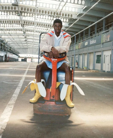 Adult male fashion model poses sitting on red forklift wearing shorts and boots with banana peels on empty loading dock.
