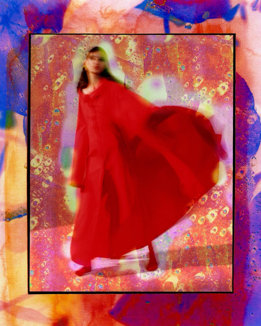 A slender adult female in a flowing red dress poses in front of an abstract colorful artistic backdrop with painterly and watercolor effects.