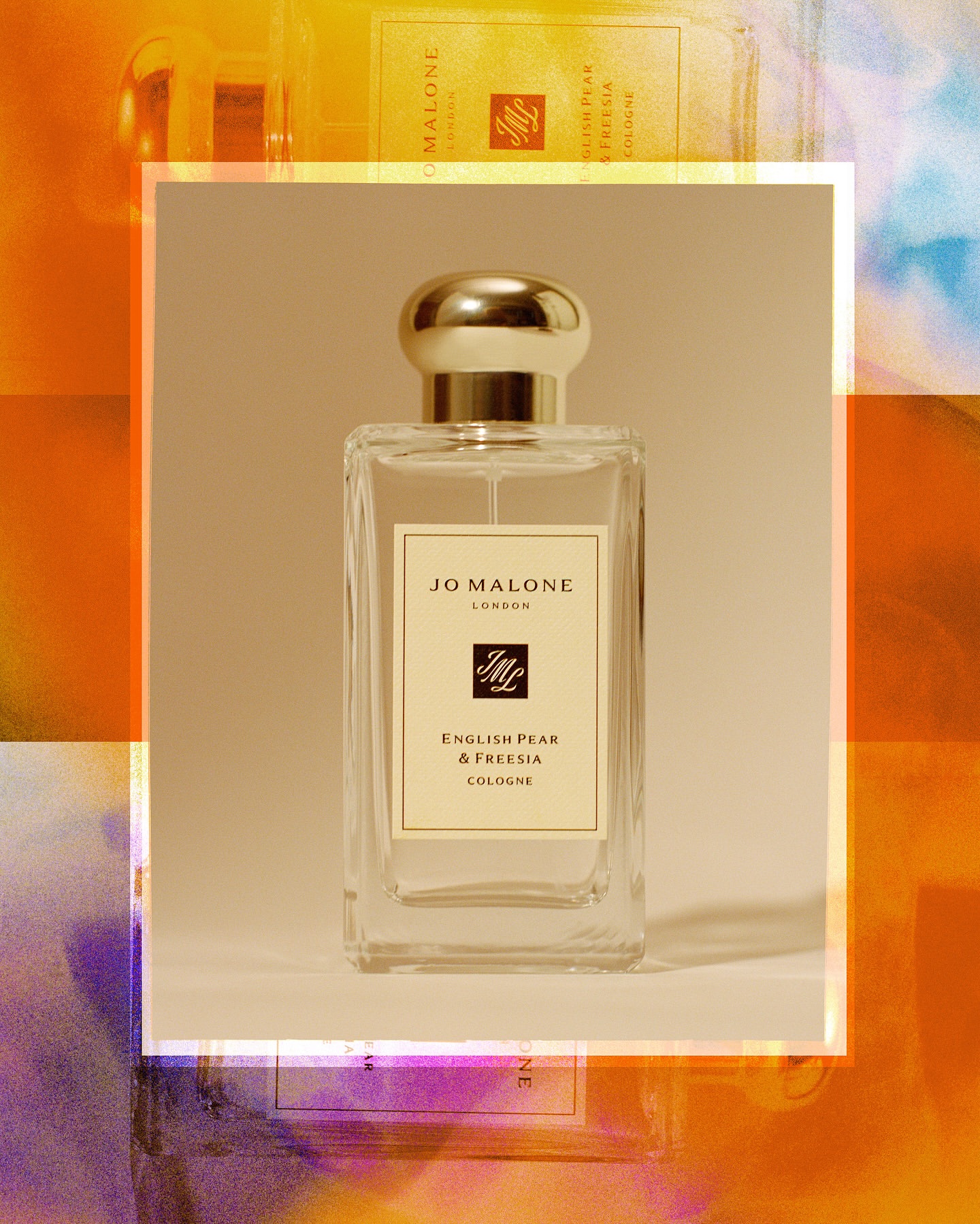 Rectangular Jo Malone London English Pear and Freesia cologne bottle with a round gold cap stands in front of a blurred backdrop.