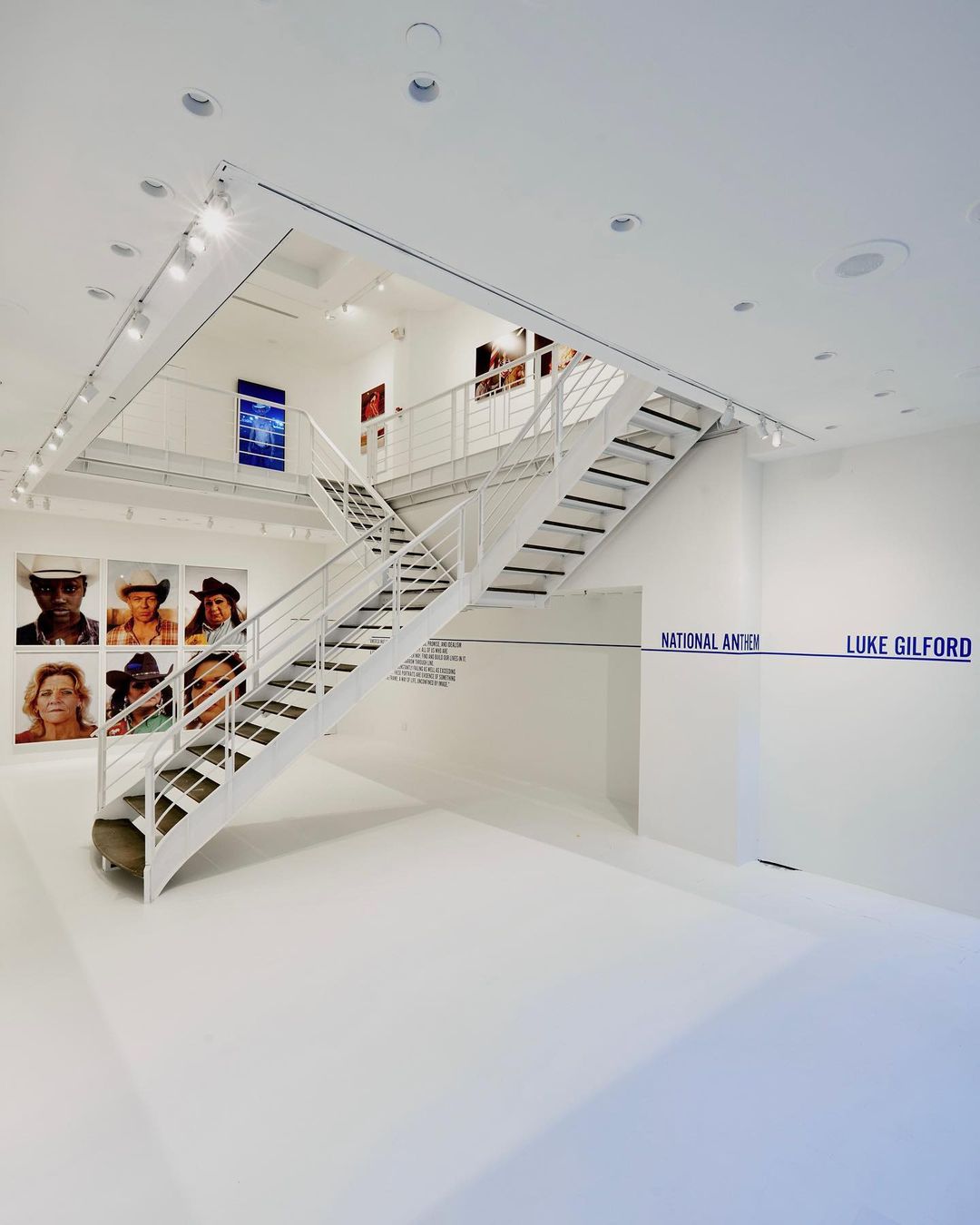 Art gallery interior featuring white walls, a metal staircase, and framed photographs on display, creating a clean and modern aesthetic.