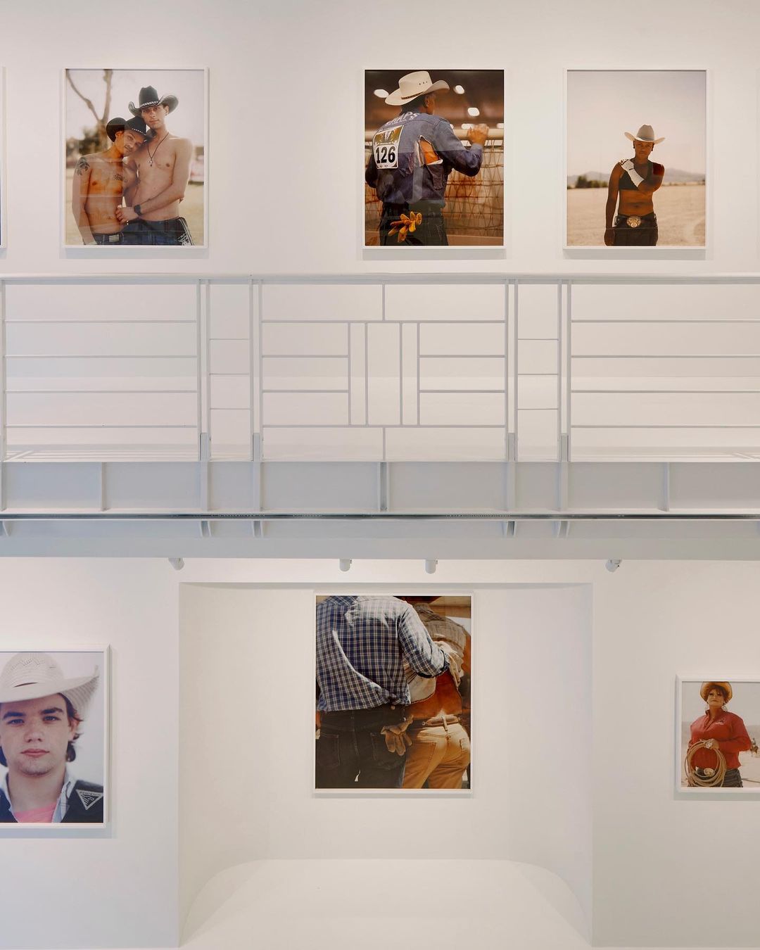 Photo gallery with framed photos of people in cowboy hats on display in a white room with a white geometric-patterned structure.