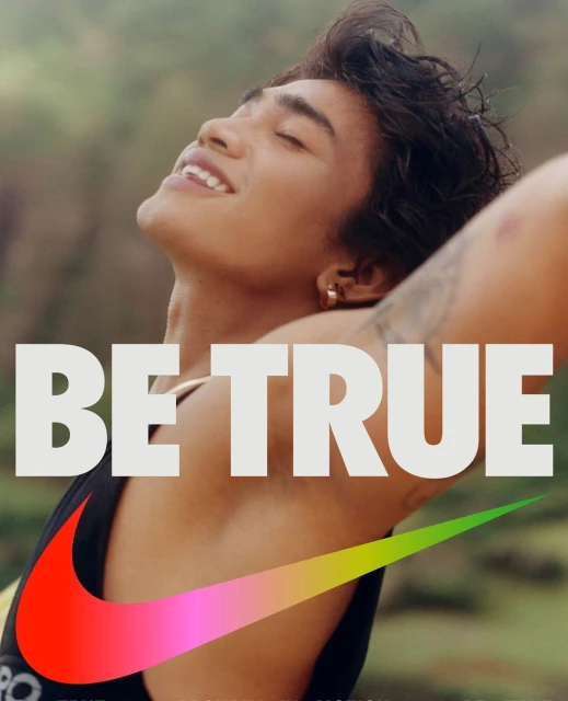 Athletic male smiles with eyes closed, wearing a tank top with the Nike logo, outdoors against a blurry green nature backdrop.