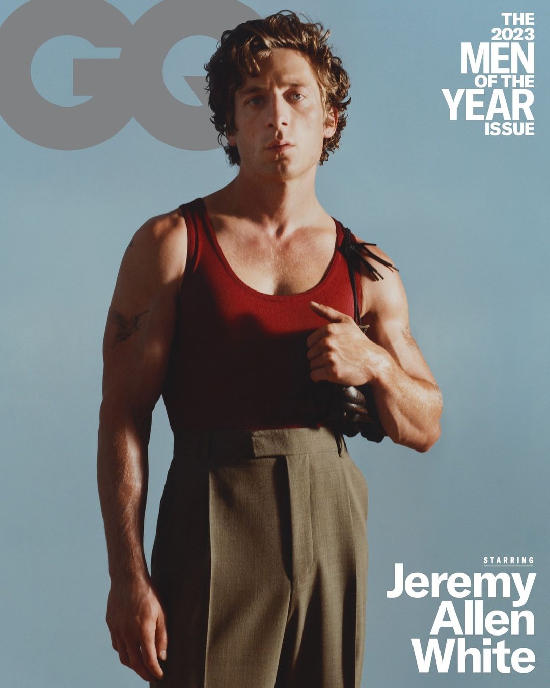 Jeremy Allen White poses in a tank top and trousers for the cover of GQ's 2023 Men of the Year issue against a clear blue backdrop.