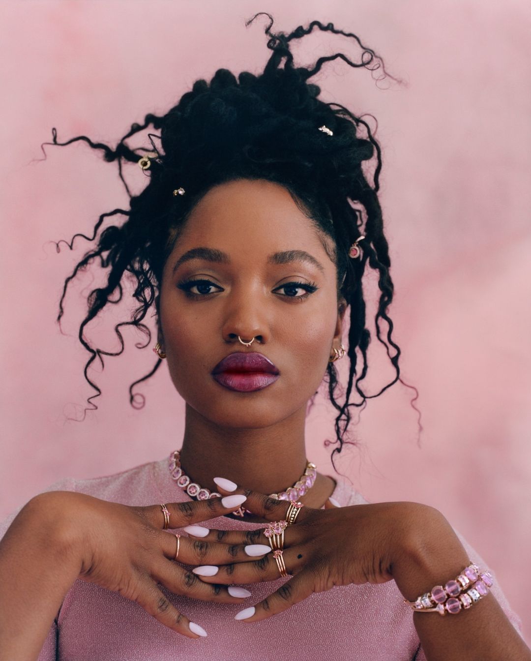 Close-up of an African-American woman with locs, wearing pink jewelry and a pink shirt against a pink backdrop. Beauty and fashion.