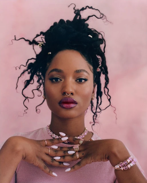 Close-up of an African-American woman with locs, wearing pink jewelry and a pink shirt against a pink backdrop. Beauty and fashion.