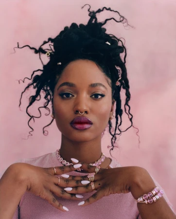 Close-up of an African-American woman with locs, wearing pink jewelry and a pink shirt against a pink backdrop. Beauty and fashion.