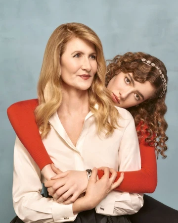 Indoor portrait of actress Laura Dern and a younger woman. The pair pose intimately in front of a simple light blue studio backdrop.