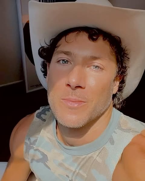 Portrait of a man wearing a cowboy hat and a camouflage shirt, with natural sunlight casting shadows across his face.