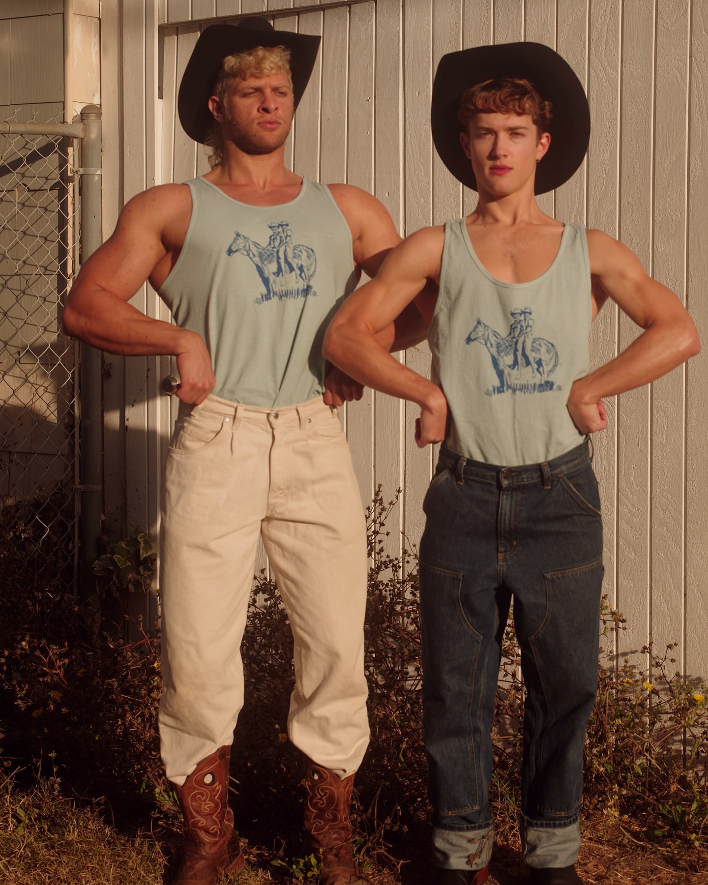Two adult males strike a pose in cowboy hats and tank tops featuring horse graphics, complemented by cowboy boots and a backyard setting.