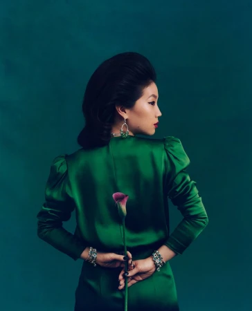 Portrait of an Asian woman in a green dress holding a calla lily against a green backdrop. The woman is seen from the back.