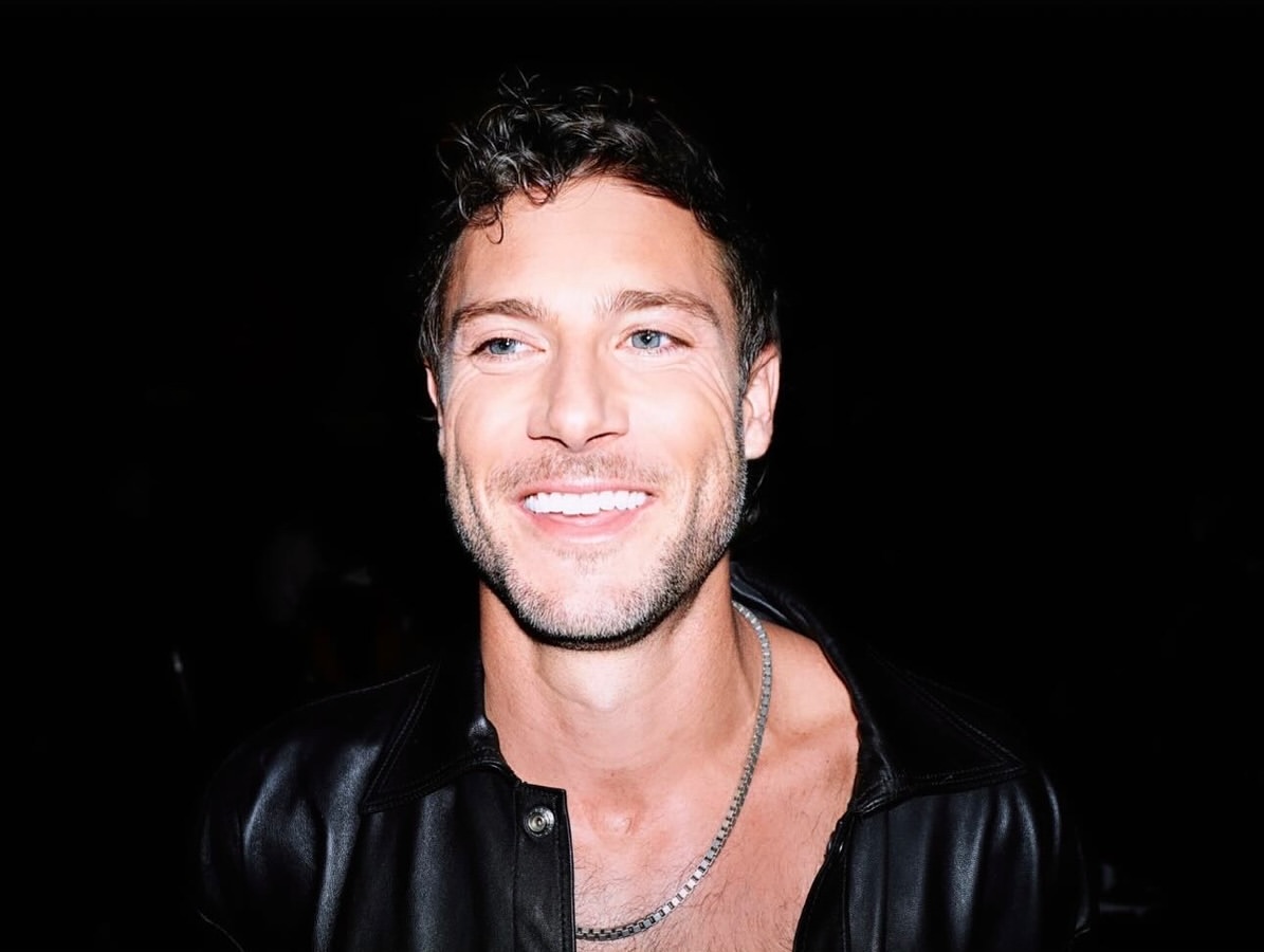 Close-up studio shot of an adult male with dark hair, tanned skin, and blue eyes, wearing a black leather jacket and silver chain.