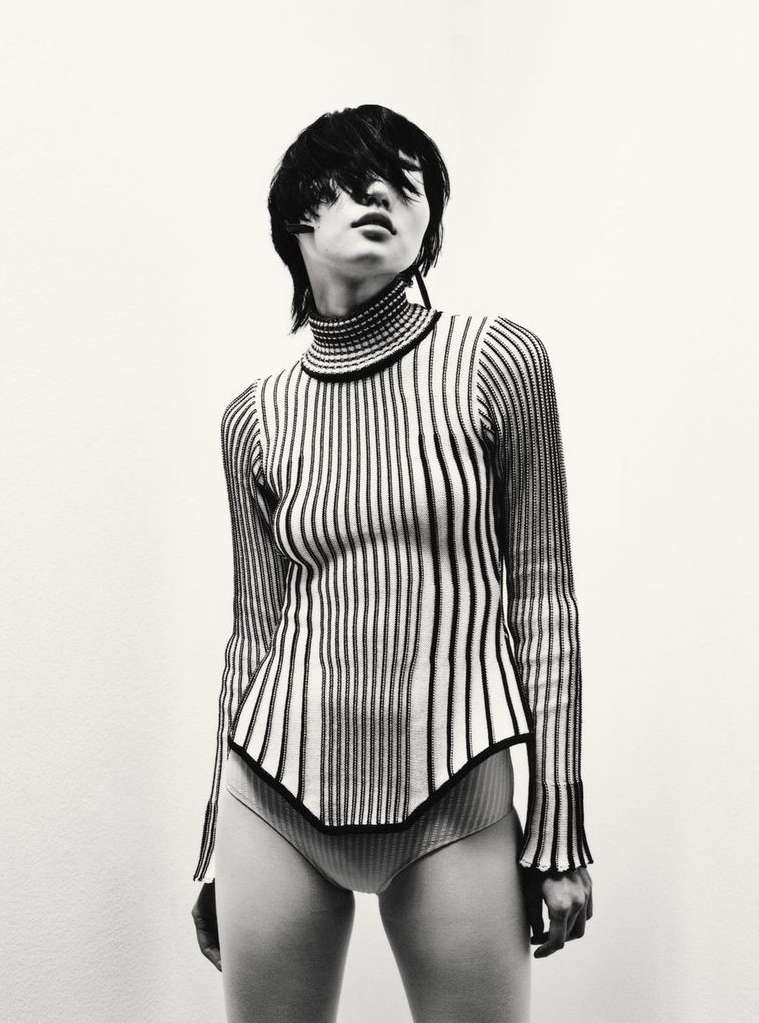 Fashion shot featuring an adult woman with short dark hair, wearing a striped turtle neck and briefs, against a plain light backdrop.