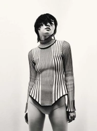 Model with dark hair wearing a striped turtleneck sweater against a plain white background