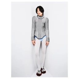 Model in a black and white striped turtleneck and white tights standing against a plain white corner backdrop