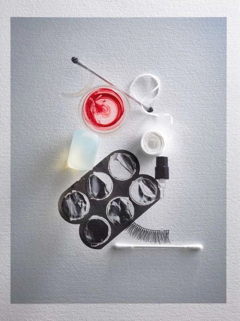 Overhead shot of beauty and makeup tools including a lip gloss, concealer palette, cleanser, lash glue, cotton swabs, and false eyelashes.