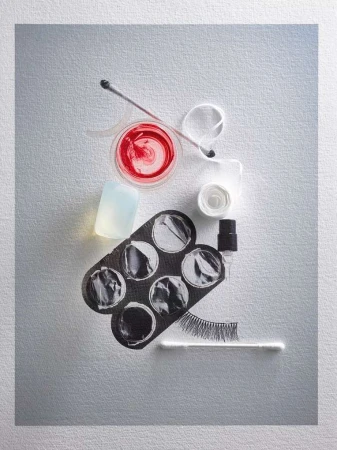Overhead shot of beauty and makeup tools including a lip gloss, concealer palette, cleanser, lash glue, cotton swabs, and false eyelashes.
