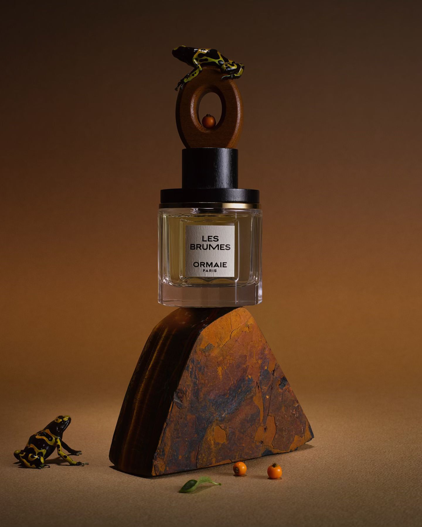 Perfume bottle on a stone display with a decorative wooden top and small frog figurines against a warm, gradient background.