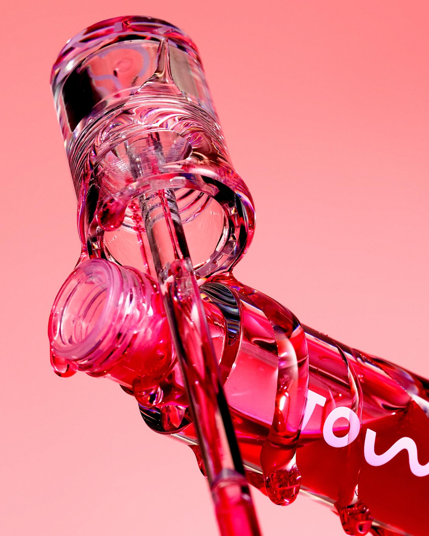 Product shot of a transparent bottle with a pink liquid on a pink background, emphasizing minimalist aesthetic and material transparency.