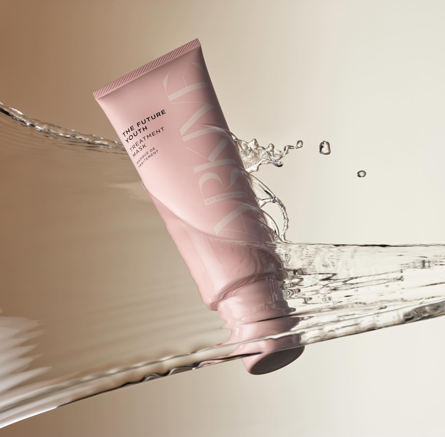 Pink tube of Arkive The Future Youth Treatment Mask product shot with splashing water against a beige background in vertical format.