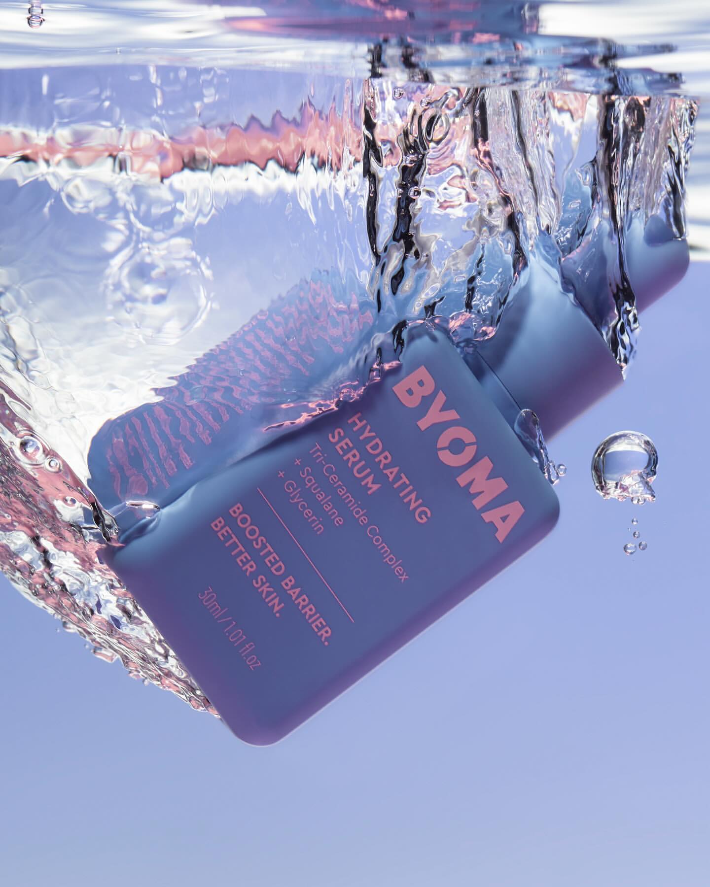 Blue Byoma hydrating serum bottle submerged underwater with splashing water and visible air bubbles